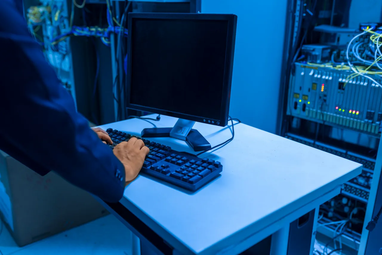 Profesional de tecnología revisando equipos y conexiones de una sala de servidores.
